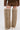 A person wears brown faux leather shorts and jacket with the AZALEA WANG LAGANN BONE THIGH HIGH FUR LUXE BOOTS styled as tall beige fur thigh-highs over white pointed-toe shoes, standing against a plain white background.