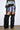 A person stands against a white background in a black mesh top with gray faux fur trim, a light purple faux fur mini skirt, and AZALEA WANG LANGLEYE BLACK THIGH HIGH FUR LUXE BOOTS.
