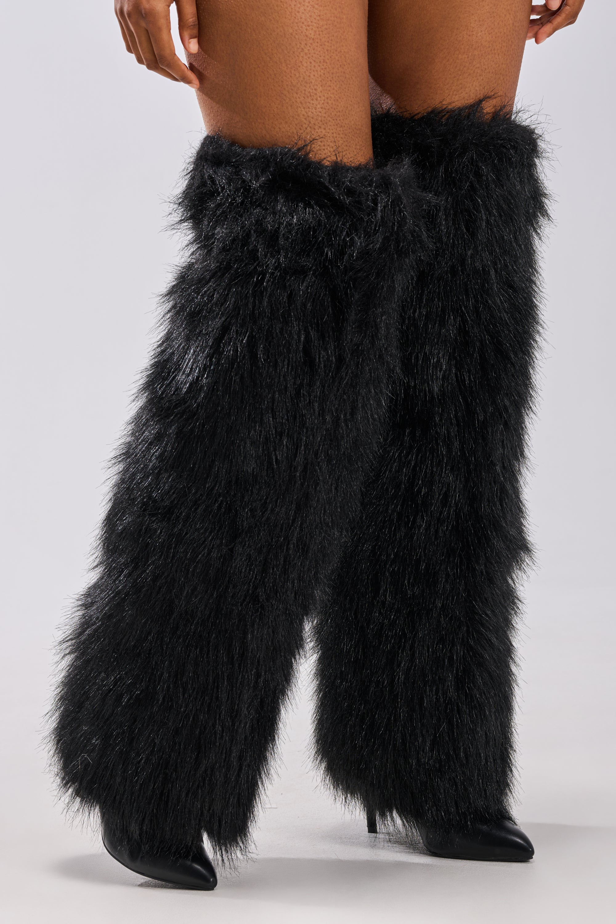 A person wears the AZALEA WANG LANGLEYE BLACK THIGH HIGH FUR LUXE BOOT, featuring knee-high black faux fur over stiletto heels, with bare thighs visible against a plain light background.