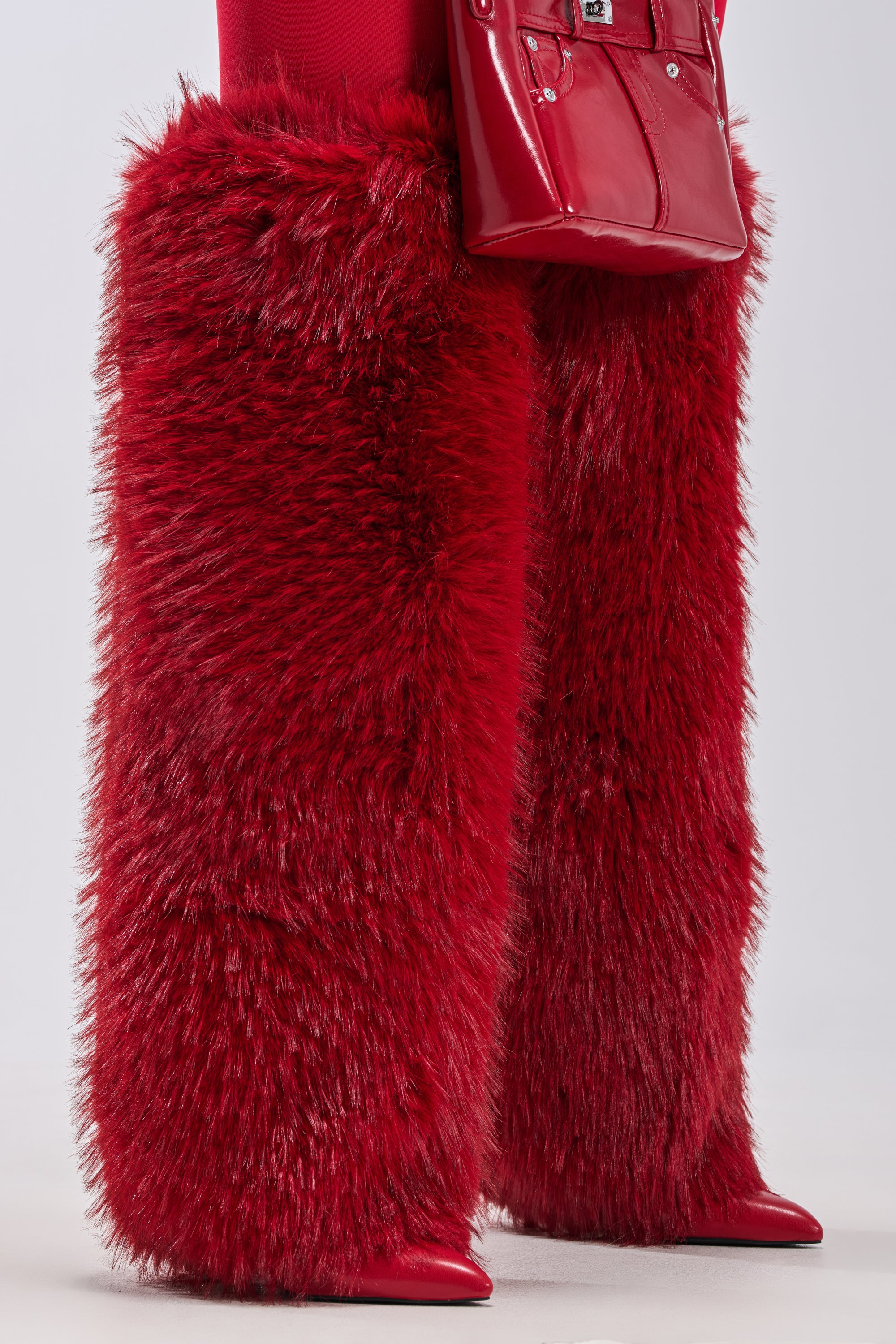 Wearing AZALEA WANG LANGLEYE RED THIGH HIGH FUR LUXE BOOTS and a shiny red handbag, a person in matching red clothing poses against a plain light background.