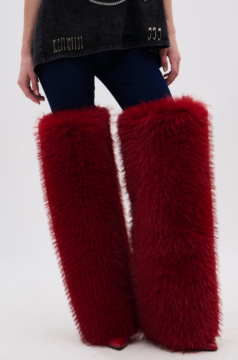 A person in dark pants and a black top with metallic details wears the AZALEA WANG LANGLEYE RED THIGH-HIGH FUR LUXE BOOT, featuring bright red fur from knee to shoe and bold stiletto heels for a striking look.