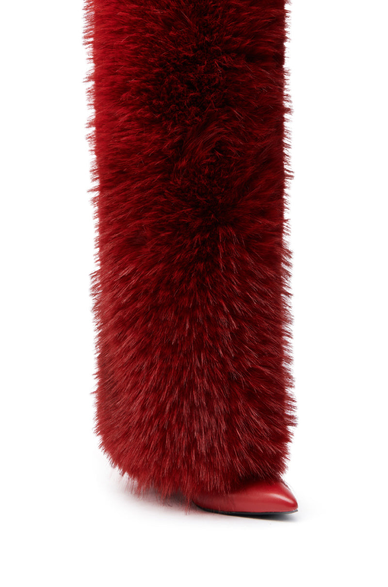 A close-up of the AZALEA WANG LANGLEYE RED THIGH-HIGH FUR LUXE BOOT shows a leg wrapped in thick red fur, with a pointed stiletto heel peeking out, creating a bold and dramatic textured look.
