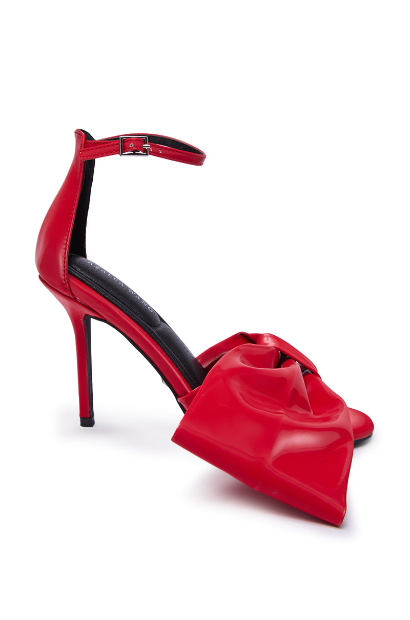 The AZALEA WANG LANYIN RED LIQUID LUXE BOW SANDAL boasts an ankle strap, a bold front bow, and a sleek stiletto heel, all crafted from luxe faux leather for a strikingly stylish look.