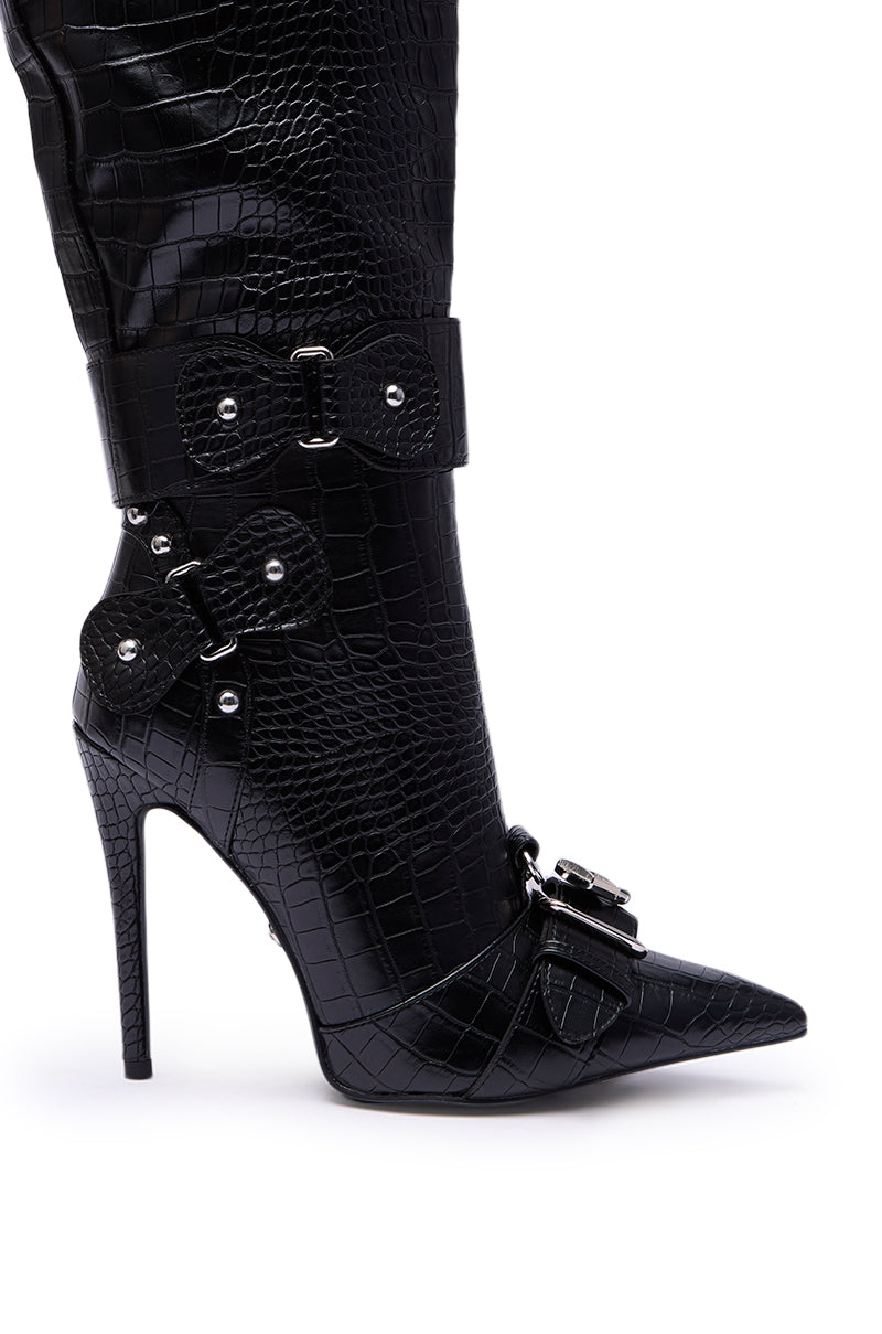 A close-up of the AZALEA WANG LAPIS BLACK SNAKE STILETO BOOT, a high-heeled, pointed-toe boot with crocodile texture, featuring decorative buckles and metal-studded straps.