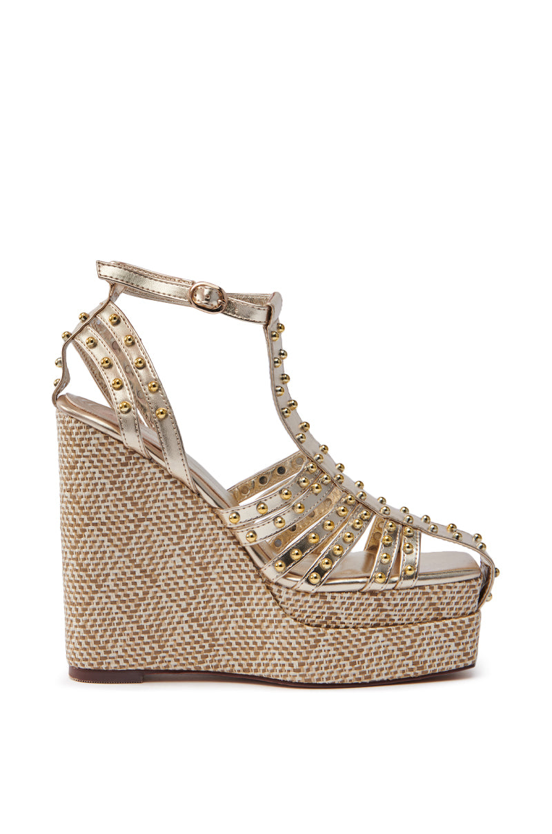 The AZALEA WANG LASZLO GOLD WEDGE SANDAL features metallic gold straps with studs, a textured wedge in brown and cream tones, and a raffia platform sole. It includes an ankle strap with a buckle closure for a secure fit.