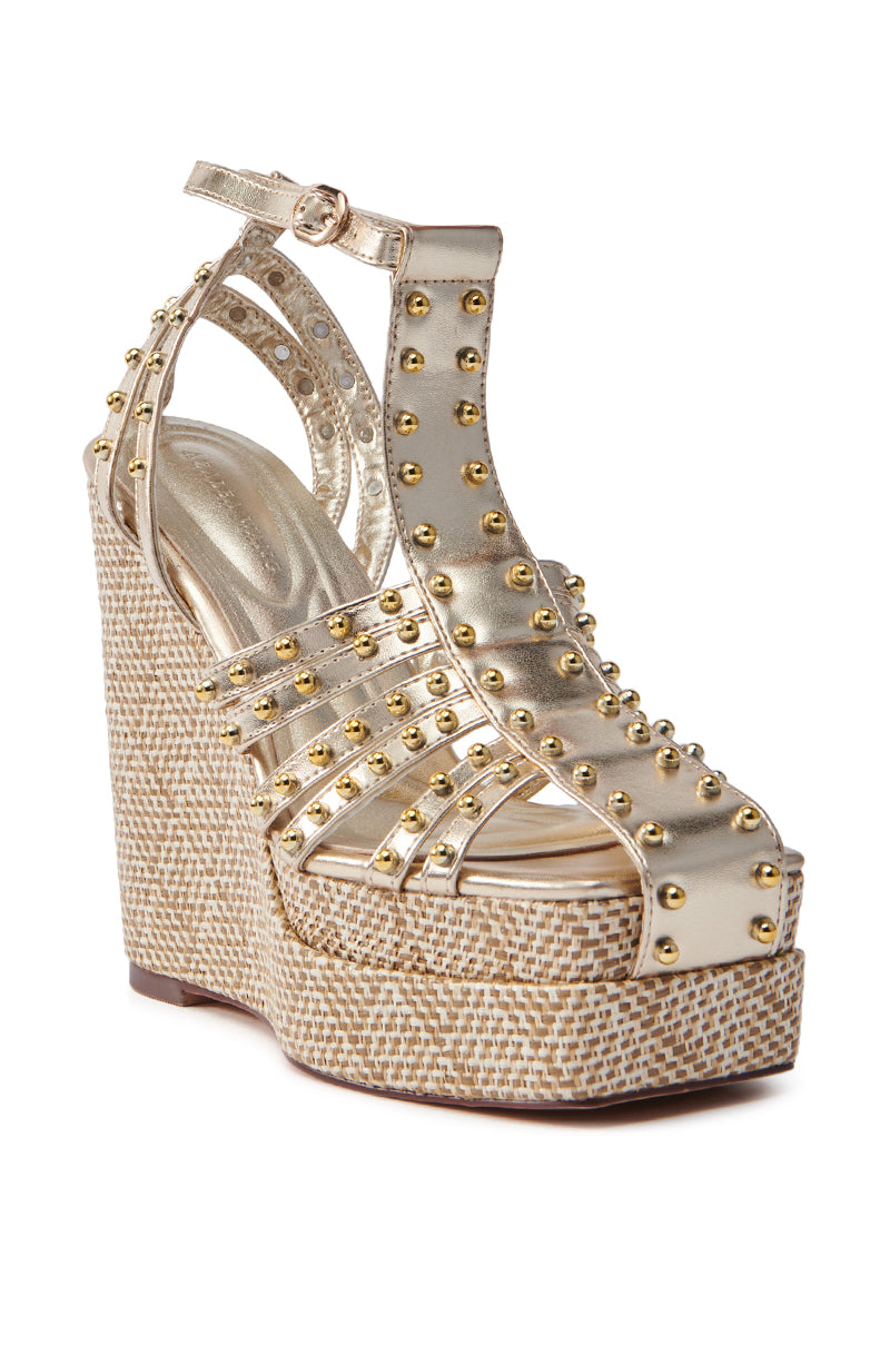 The AZALEA WANG LASZLO GOLD WEDGE SANDAL features metallic gold straps, an adjustable ankle buckle, and a raffia platform sole with woven straw texture, offering a glamorous touch to any outfit.