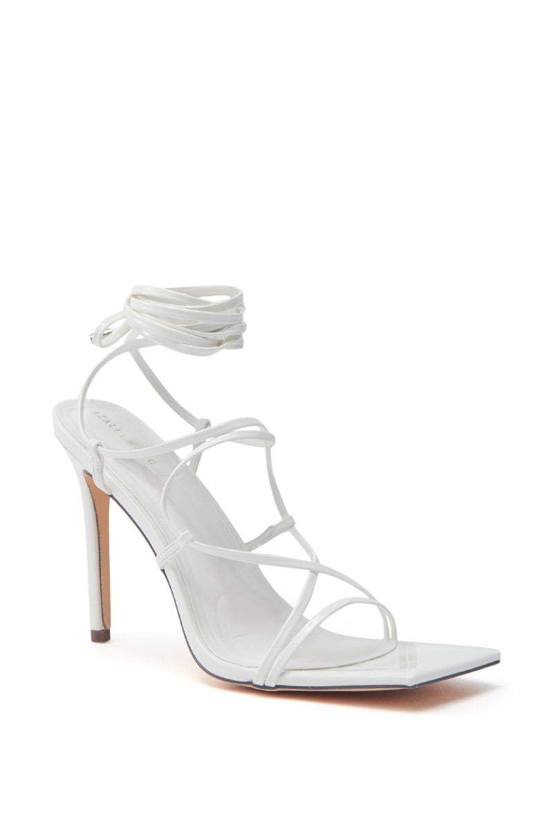 The AZALEA WANG LAURA WHITE STILETTO SANDAL features faux leather, thin adjustable crisscross straps, an ankle tie, pointed toe, and sleek stiletto heel, shown against a plain white background.