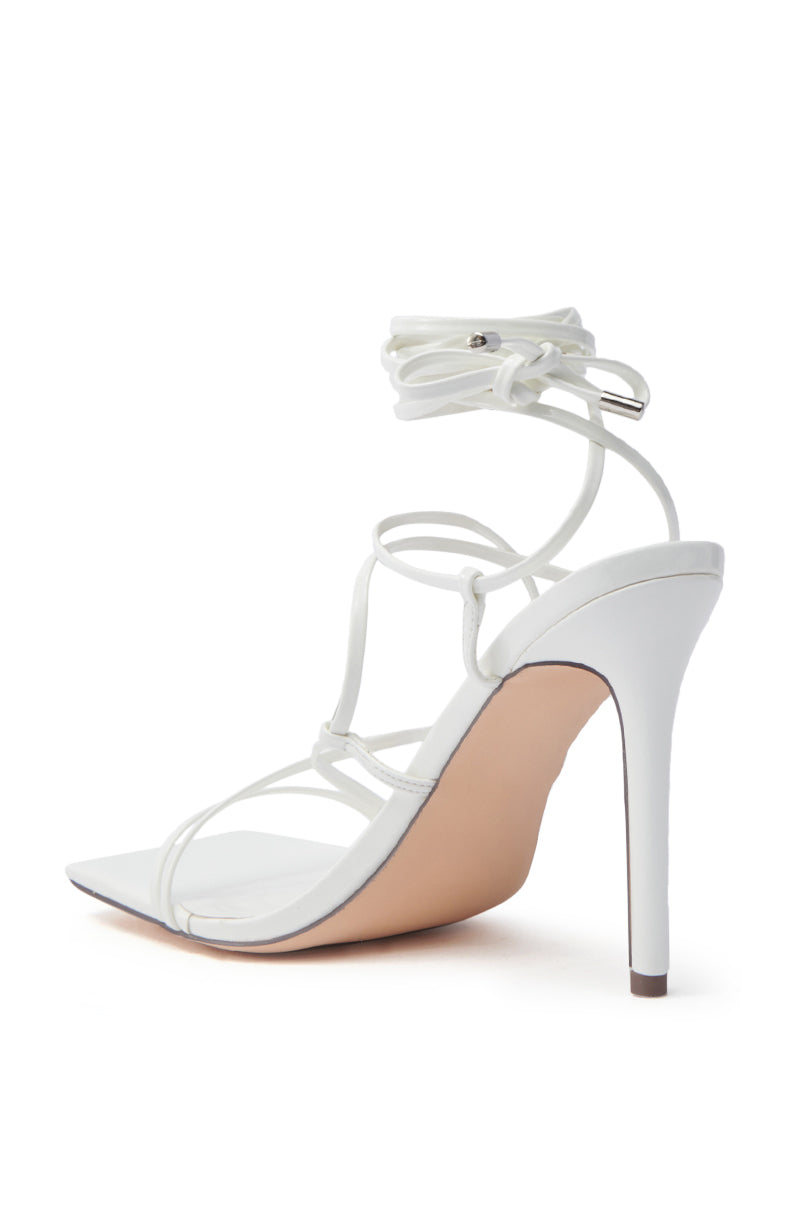 The AZALEA WANG LAURA WHITE STILETTO SANDAL features faux leather, thin adjustable straps with an ankle wrap tie, a pointed toe, and a sleek high heel, all showcased against a white background.