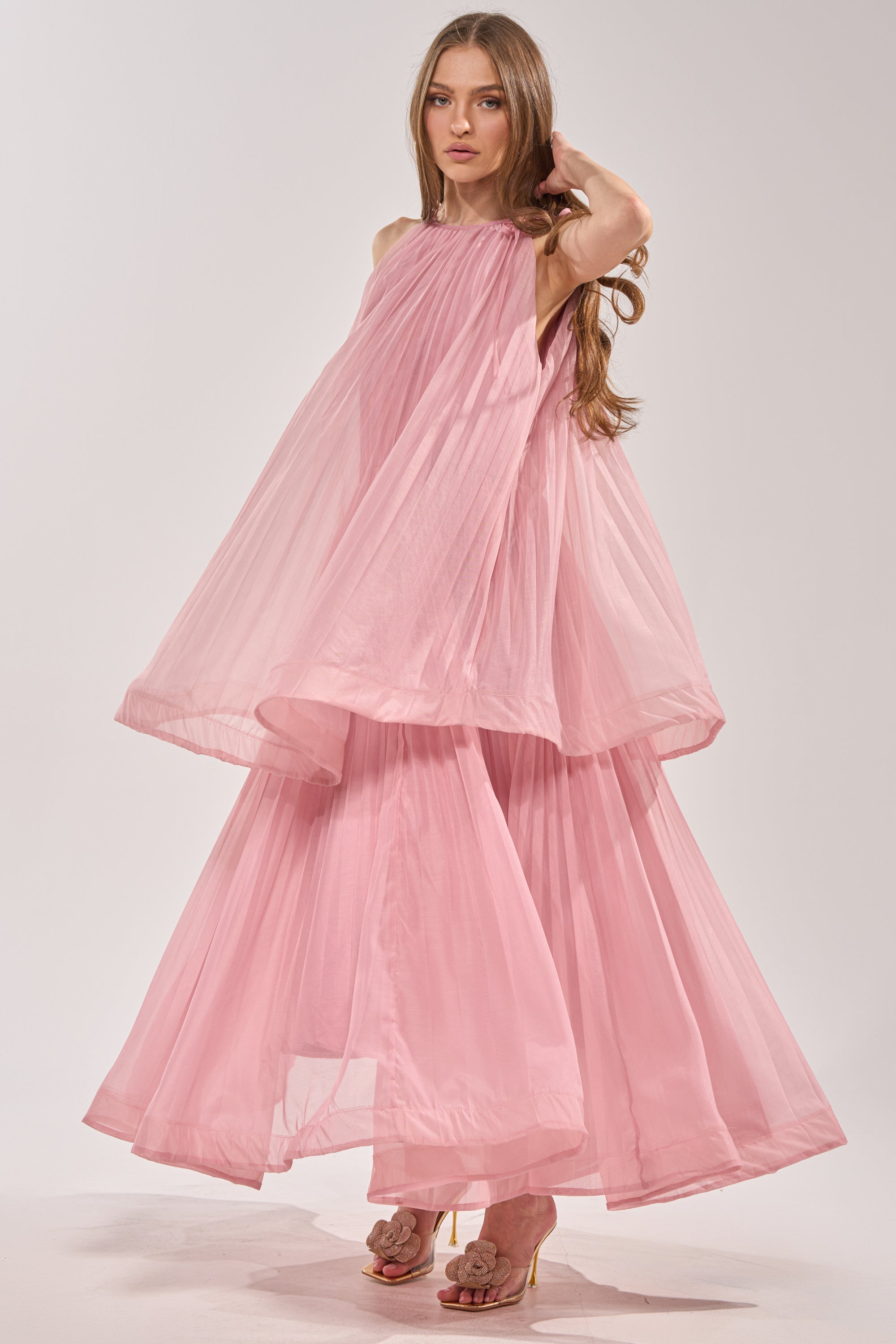A woman with long brown hair wears the BREEZY GIRL TIERED MAXI DRESS IN BLUSH and gold high-heeled sandals, posing gracefully against a plain light background. 4