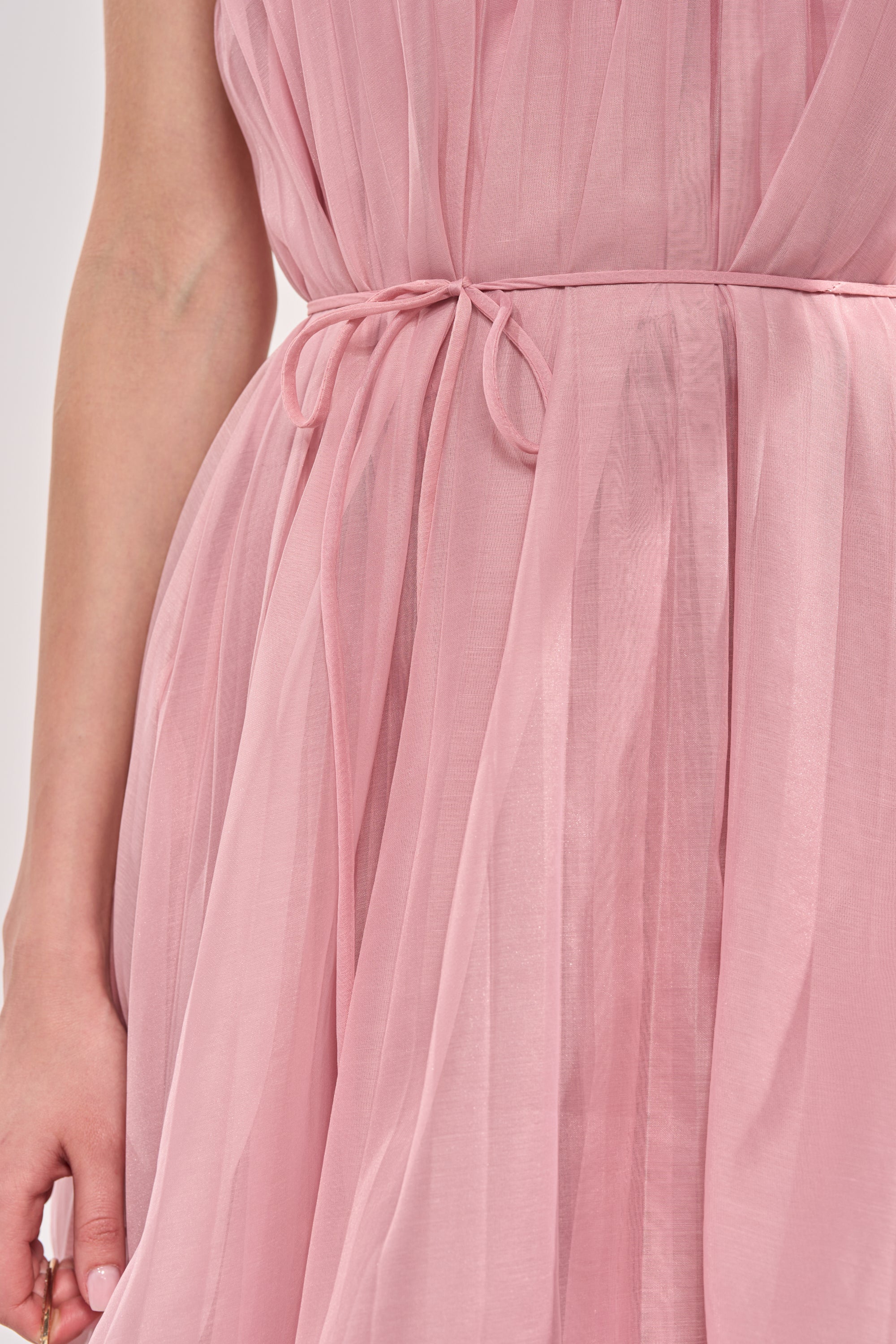 A close-up of a person wearing the BREEZY GIRL TIERED MAXI DRESS IN BLUSH, a pleated chiffon maxi with a thin waist tie. Their left hand is visible at their side. 7