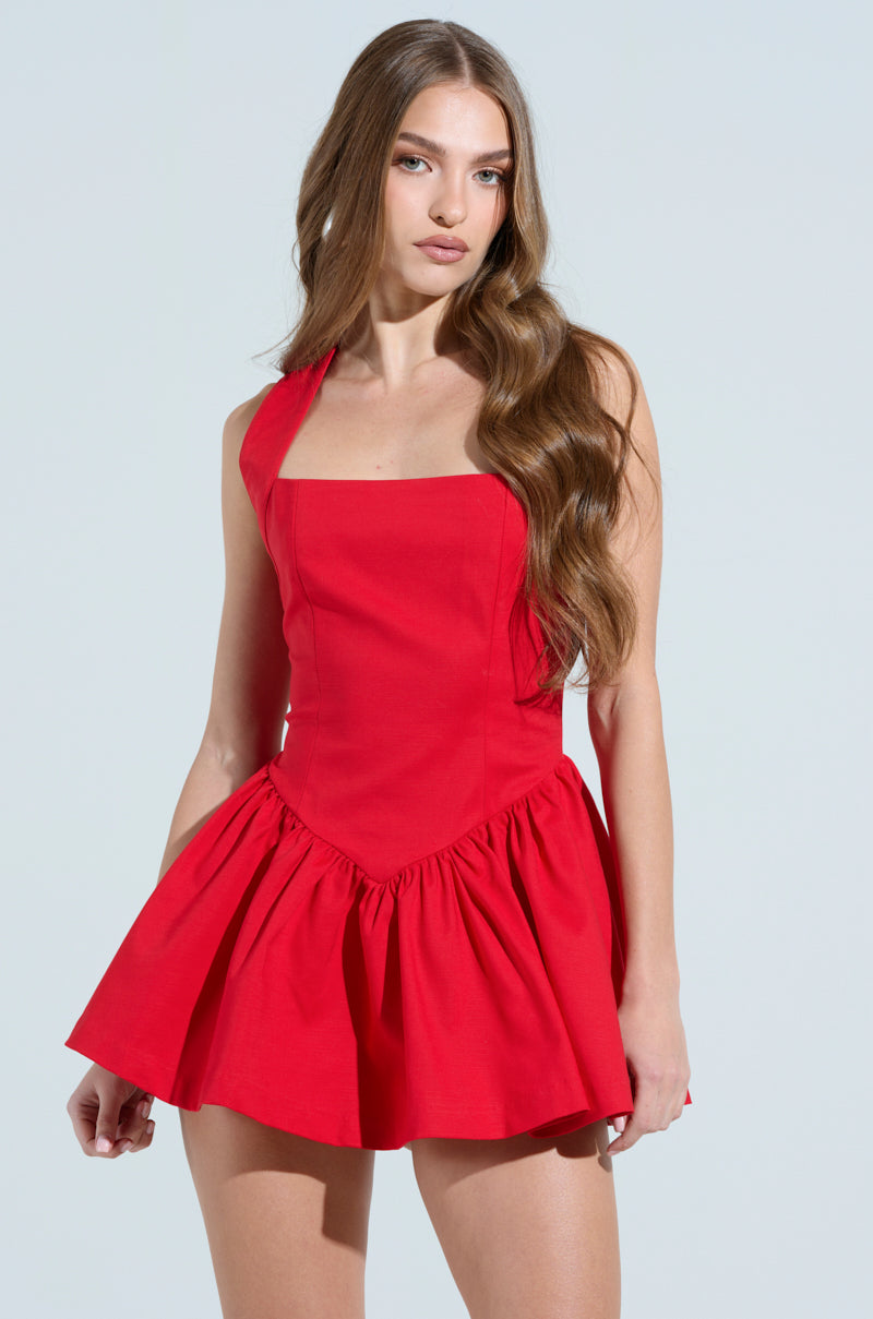 A woman with long brown hair wears the Rosalia Stretch Linen Mini Dress in red, featuring a square neckline and flared skirt. She stands against a light background, looking directly at the camera, embodying its charm.