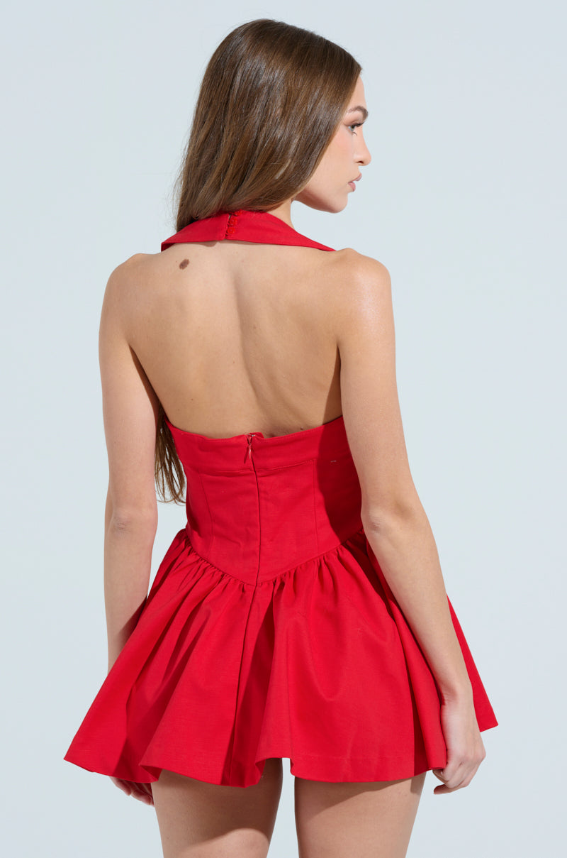 A woman with long brown hair is wearing the Rosalia Stretch Linen Mini Dress in red, featuring a sleeveless halter neck, open back, flared skirt, and zipper closure. She faces away against a plain white background.