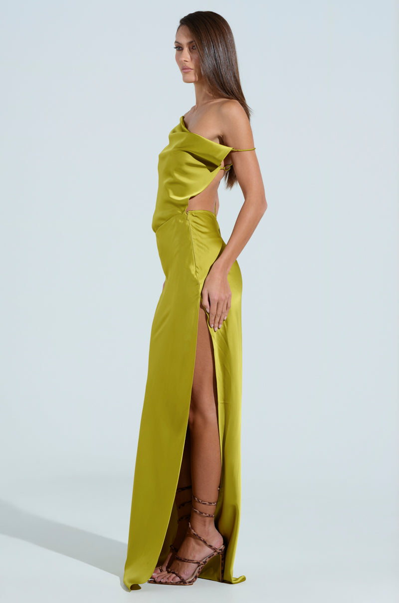 A woman in chartreuse poses with her left side facing the camera wearing the ISLA SATIN MAXI DRESS, showcasing its asymmetrical off-the-shoulder design, side cutouts, and high slit. She pairs it with strappy sandals and her long hair is styled straight.