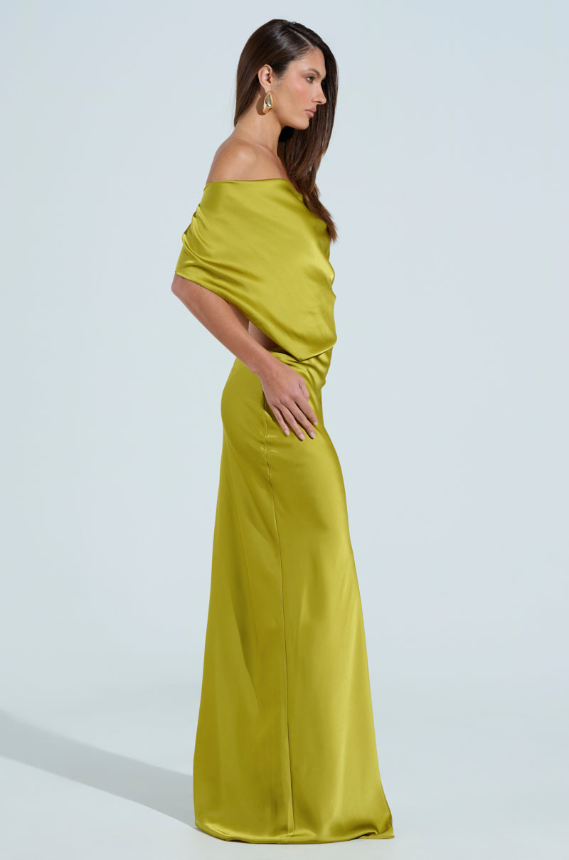 In a chartreuse satin off-the-shoulder, floor-length dress, a woman with long dark hair poses elegantly in profile against a plain backdrop. Wearing hoop earrings and resting her right arm on her hip, she beautifully showcases the ISLA SATIN MAXI DRESS.