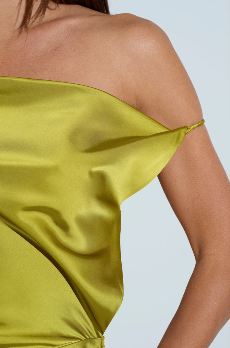 Close-up of a person in a lime-green satin, asymmetrical off-the-shoulder dress similar to the ISLA SATIN MAXI DRESS, with fabric draping over one shoulder and highlighting the chartreuse sheen against light skin.
