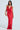 The woman, elegantly dressed in the SEXY CAN I SATIN MAXI DRESS featuring a cowl neckline and thigh-high slit, holds a small gold clutch. Against a plain white background, she showcases her sophisticated style.
