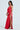 A woman in the SEXY CAN I SATIN MAXI DRESS, with a cowl neckline and thigh-high slit, poses against a plain backdrop. She accessorizes with a small clutch and strappy high heels, her dark hair styled in soft waves.
