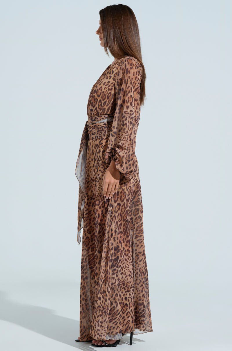 A woman with long brown hair is seen in profile, wearing the RYAN LEOPARD PRINT MAXI DRESS featuring balloon sleeves, paired with black heels. The backdrop is a light gray.