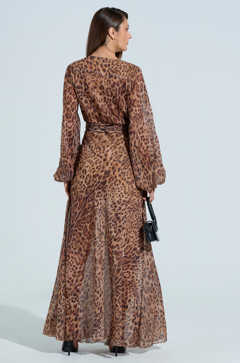 A woman is wearing the RYAN LEOPARD PRINT MAXI DRESS, featuring balloon sleeves, paired with black high heels and a small black handbag. Facing away, the dress elegantly flows around her.