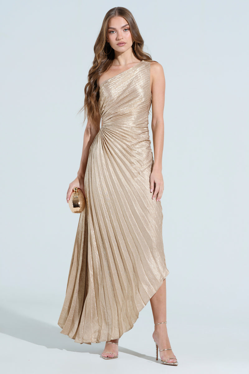 Wearing the Juliette Metallic Pleated Midi Dress, a woman poses against a light blue background. The gold one-shoulder gown has an asymmetrical hem and flowing skirt, paired with a small clutch and strappy heels. Her long, wavy hair cascades over her shoulder.