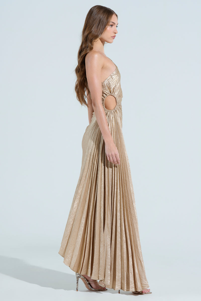 In profile against a light backdrop, a woman wears the JULIETTE METALLIC PLEATED MIDI DRESS with a side cutout, complemented by high heels, her long hair flowing elegantly down her back.