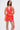 A woman stands with her arms behind her back, modeling the ROXANNE PRINTED MINI DRESS—sleeveless, halter-neck, open back, and asymmetrical hem—against a plain white background.