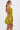 A woman in profile wears the STAR OF THE SHOW SATIN MINI DRESS, a shiny chartreuse satin mini with a flared skirt and halter neckline. She styles her long, straight ponytail with gold statement earrings.