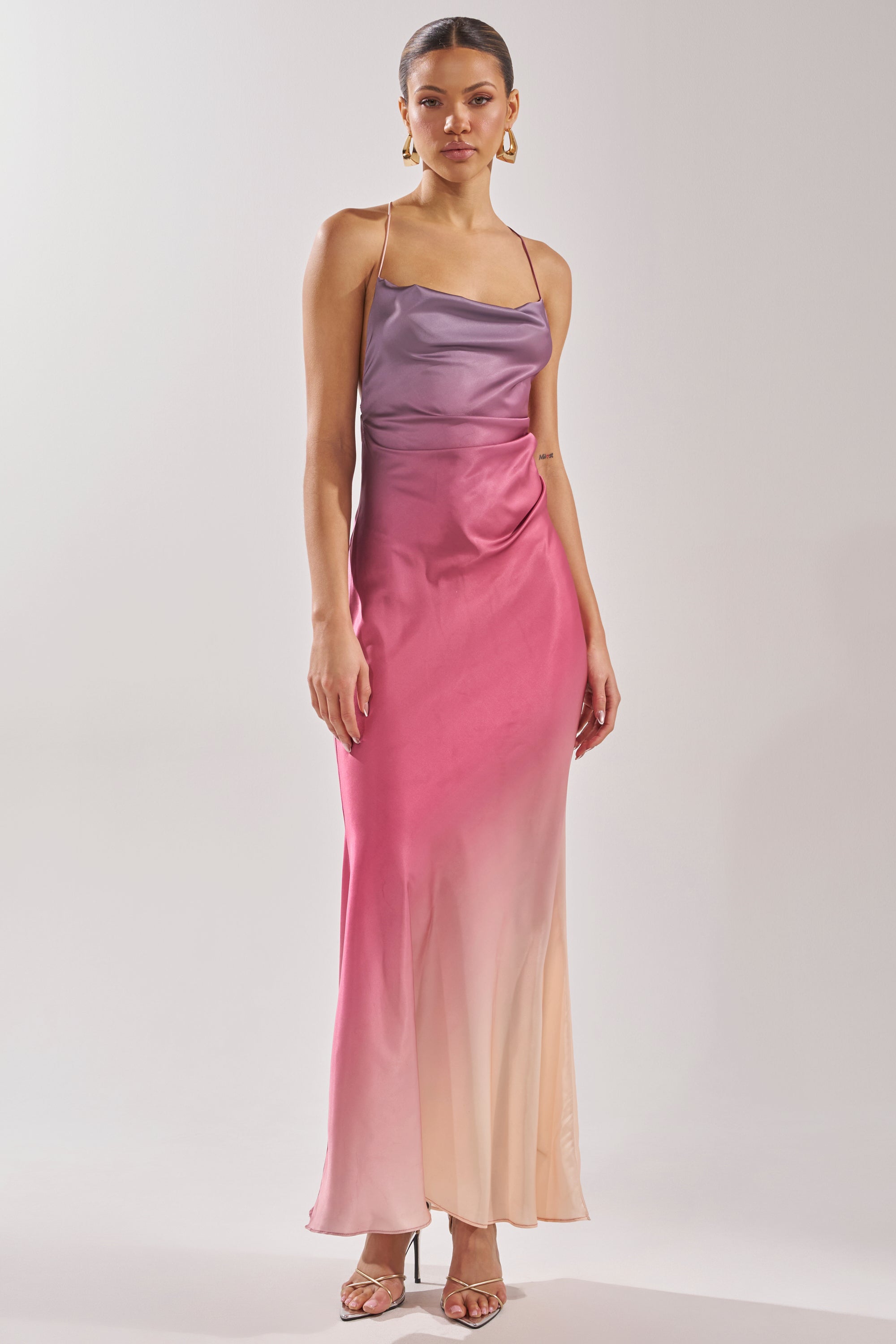 A woman wears the PRETTY WOMAN MAUVE MAXI DRESS, a sleeveless, floor-length satin gown with thin straps and an ombre gradient fading from purple to pink and light beige. 1