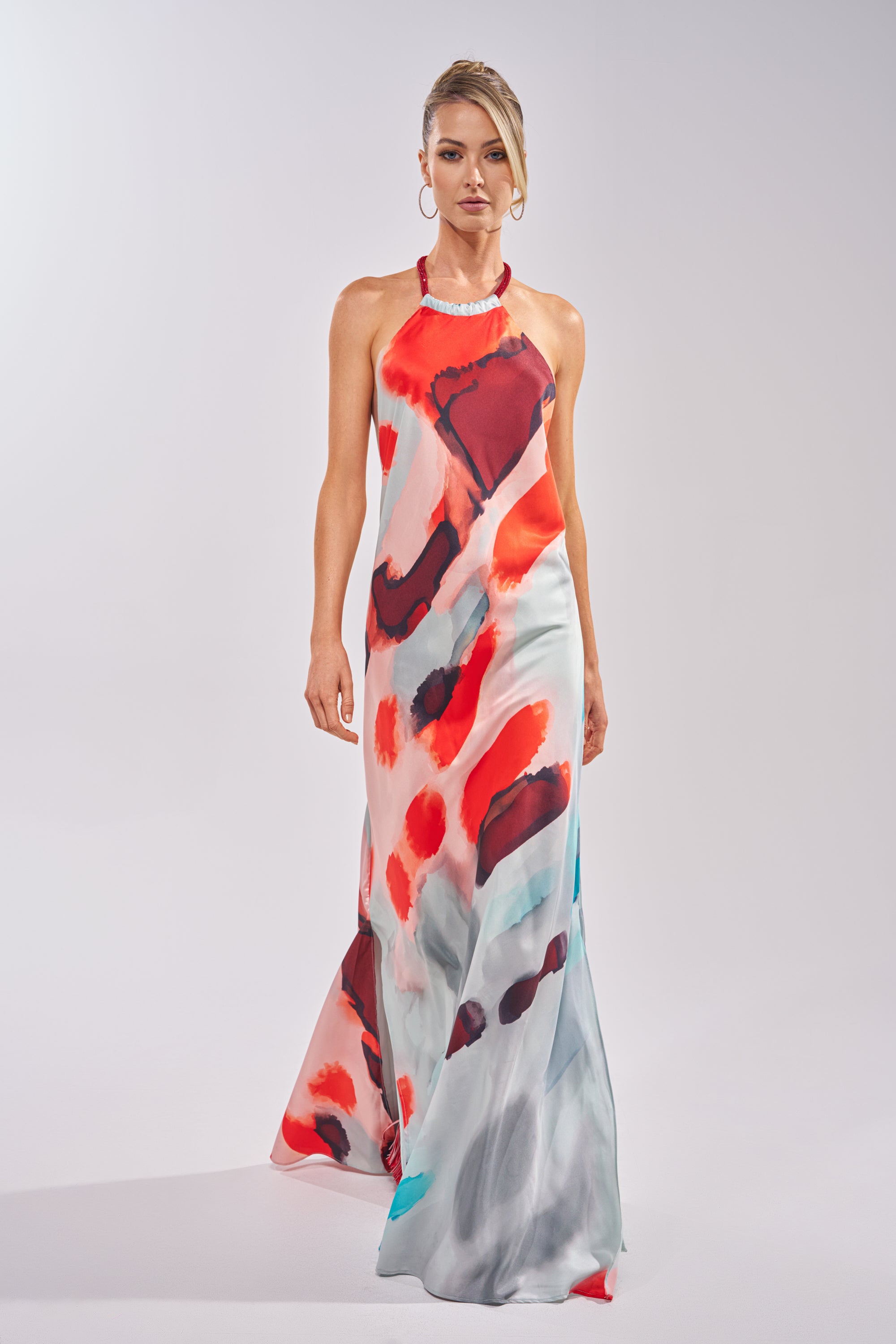A woman confidently faces forward against a plain light background, wearing the CHIC IS ME Satin Maxi Dress in Multi, which features an abstract print with bold red, black, and blue patterns. 2