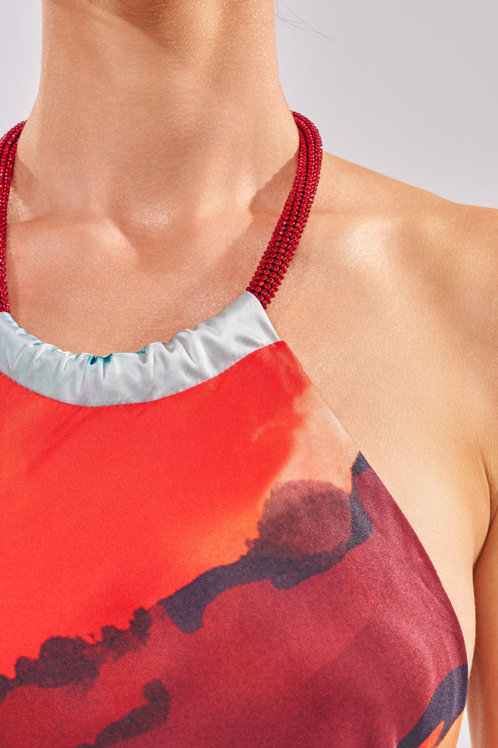 A close-up of a person wearing the CHIC IS ME Satin Maxi Dress in Multi, featuring an abstract red and orange print and a beaded red neckline, set against a neutral background. 5