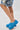 A person wears the AZALEA WANG LEESHA BLUE PONY HAIR CHUNKY CLOG slip-ons with denim shorts, standing against a white background. Only their legs and part of the shorts are visible.