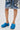 A person wearing patchwork denim shorts and blue AZALEA WANG LEESHA PONY HAIR CHUNKY CLOGS with a furry finish stands on a white surface. The photo is cropped to show only the legs and feet.