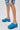 Person wearing distressed denim shorts stands on a plain white surface, showcasing the AZALEA WANG LEESHA BLUE PONY HAIR CHUNKY CLOG. Only their legs and feet are visible, highlighting these standout summer slip-ons in a stylish look.