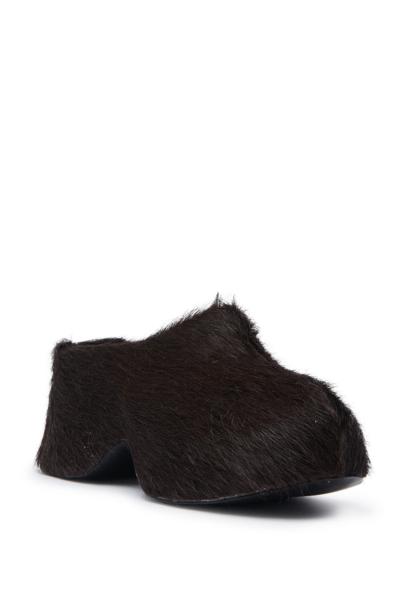 The AZALEA WANG LEESHA CHOCOLATE PONY HAIR CLOG is a modern slip-on with a chunky heel, covered in dark brown faux fur pony hair, shown against a plain white background.