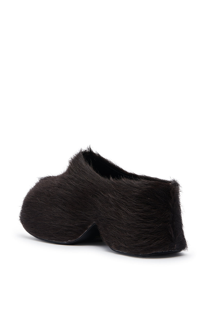 The AZALEA WANG LEESHA CHOCOLATE PONY HAIR CLOG is a slipper-style shoe with dark brown fur, shown from an angled side view against a white background, and features an easy slip-on fit.