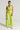 A person poses against a plain backdrop, styled in a vibrant lime green ensemble featuring the SWEET AND SPICY TANK and matching cropped wide-legged pants. They accessorize with a small silver beaded handbag and metallic silver ankle boots. Their sleek hairstyle is accented by a necklace.