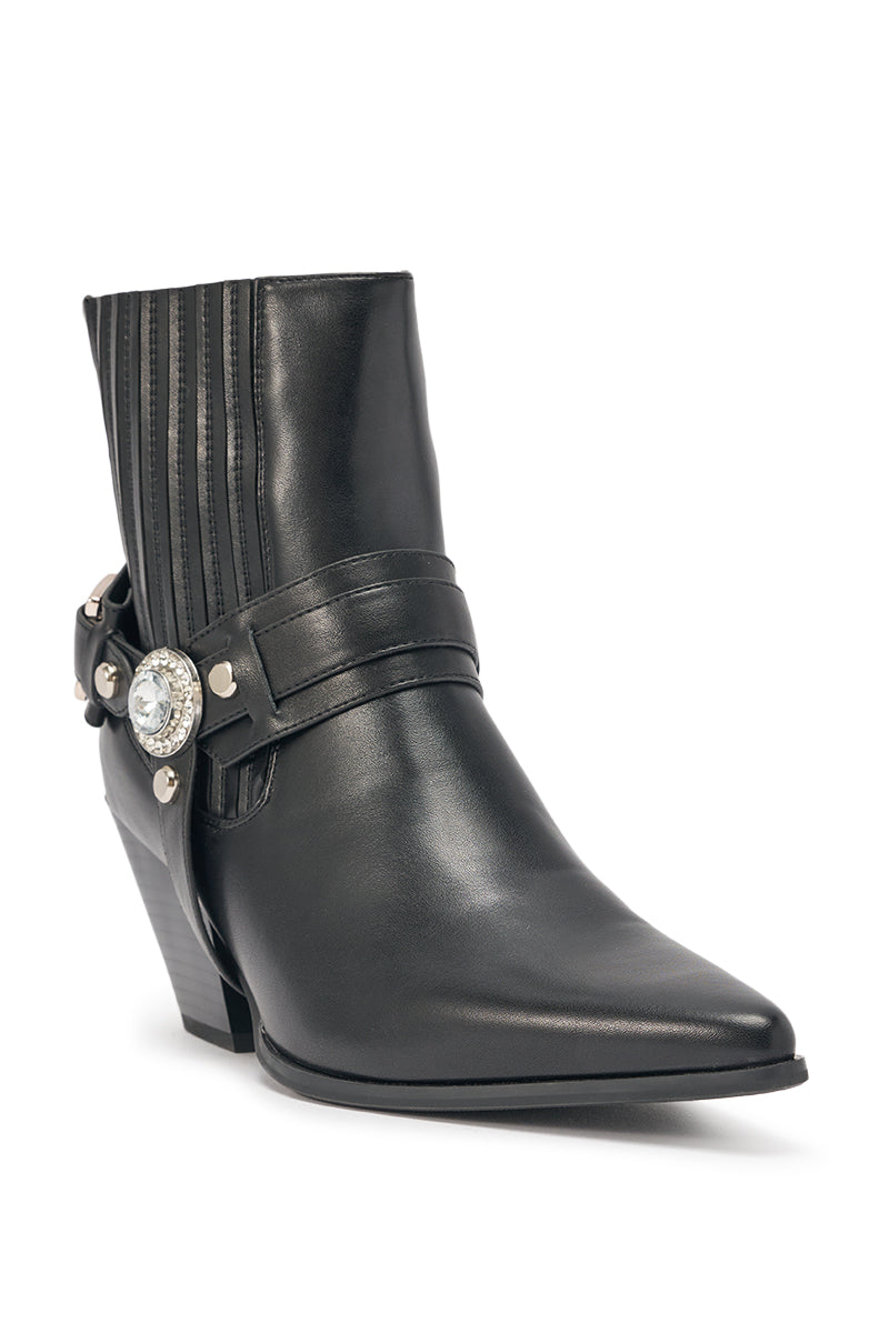 The AZALEA WANG LENKOV BLACK WESTERN BOOT features black faux leather, a pointed toe, angled chunky heel, ribbed side panel, and a bold strap with a large round jewel and metal studs for standout western style. 5