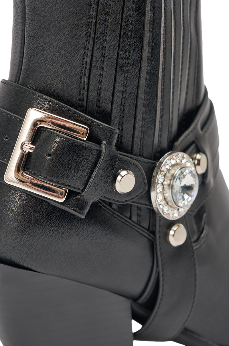 Close-up of the AZALEA WANG LENKOV BLACK WESTERN BOOT, an ankle-high black leather bootie with a silver buckle, vertical stitching, and a round jeweled ornament featuring a large central gem surrounded by smaller stones. 7