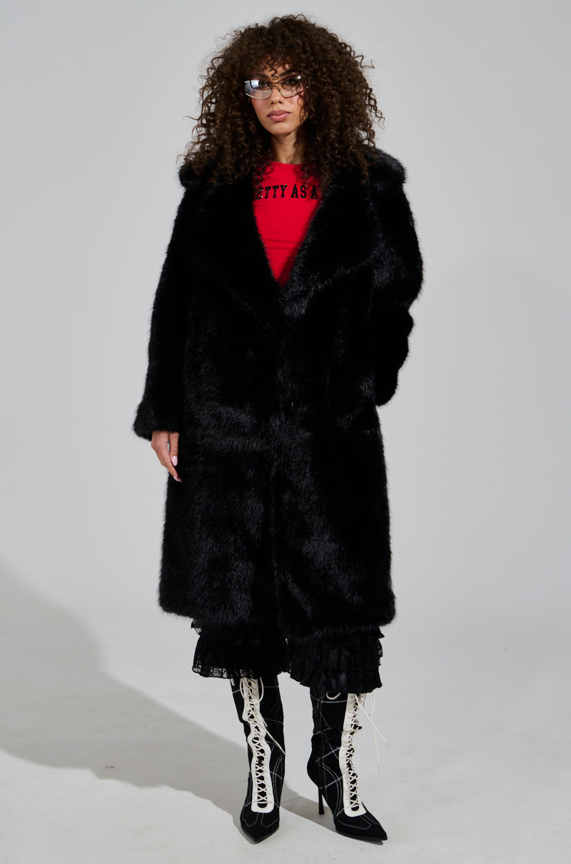 The person is dressed in the elegant LENOX Faux Fur Trench in black over a red shirt and black skirt, with curly hair and glasses. They wear chic black and white knee-high lace-up boots and pose gracefully against a light gray background.