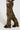 A person stands confidently against a plain background, wearing THE ULTIMATE LEOPARD CARGO PANT with a relaxed silhouette and multiple pockets, along with black chunky shoes. Their arms are crossed, perfectly showcasing the striking leopard print design of their outfit.
