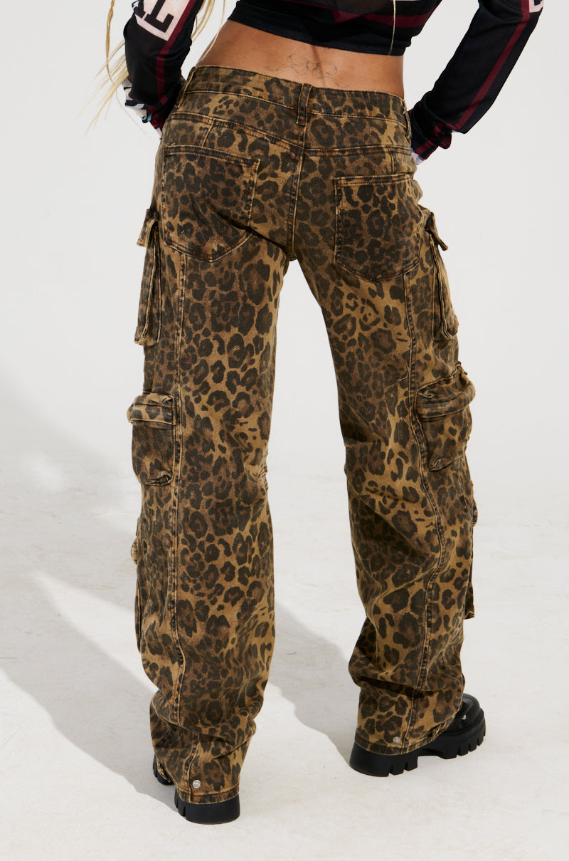 Dressed in THE ULTIMATE LEOPARD CARGO PANT with a relaxed silhouette, featuring a loose fit and multiple pockets, and complemented by black chunky boots, the individual stands facing away. Their top showcases a black and red color scheme against a plain white background.