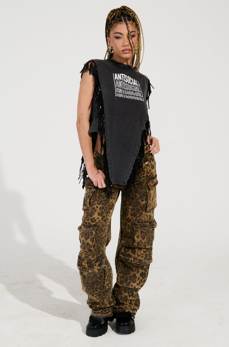 A person stands confidently wearing a sleeveless black top with text and fringe details, paired with THE ULTIMATE LEOPARD CARGO PANT in a relaxed silhouette and black boots. They have braided hair and are posing against a plain white background.