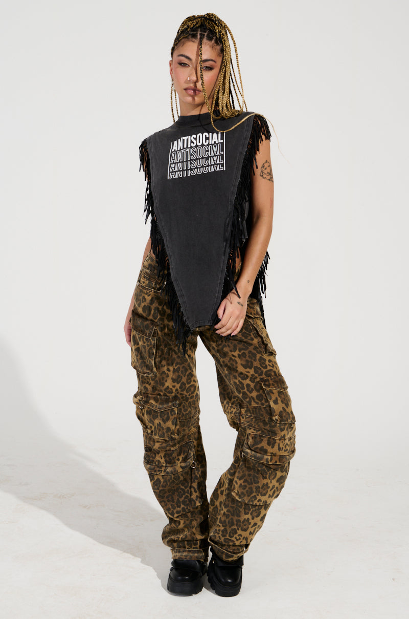 A person with braided hair stands confidently, wearing a sleeveless top featuring text and fringe details. They pair it with THE ULTIMATE LEOPARD CARGO PANT and black shoes, creating a relaxed silhouette against the plain white background.