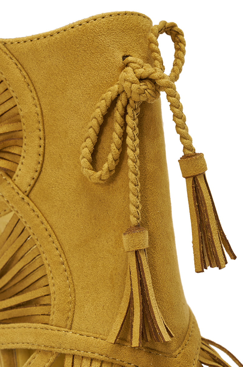 Close-up of the AZALEA WANG LEONTINE Warm Olive Wedge Faux Suede Sandal featuring braided tassel ties, decorative fringe, and a stylish platform sole. The faux suede texture and intricate braid detail are clearly visible. 6