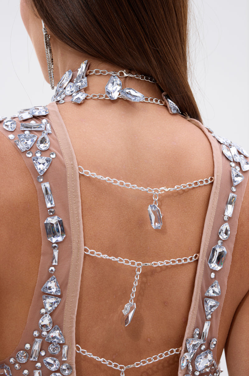 A close-up of a woman's back wearing the ALL THE BLING RHINESTONE OPEN BACK TOP, featuring sheer mesh, large clear rhinestones, and layered silver chains draped across her open back.
