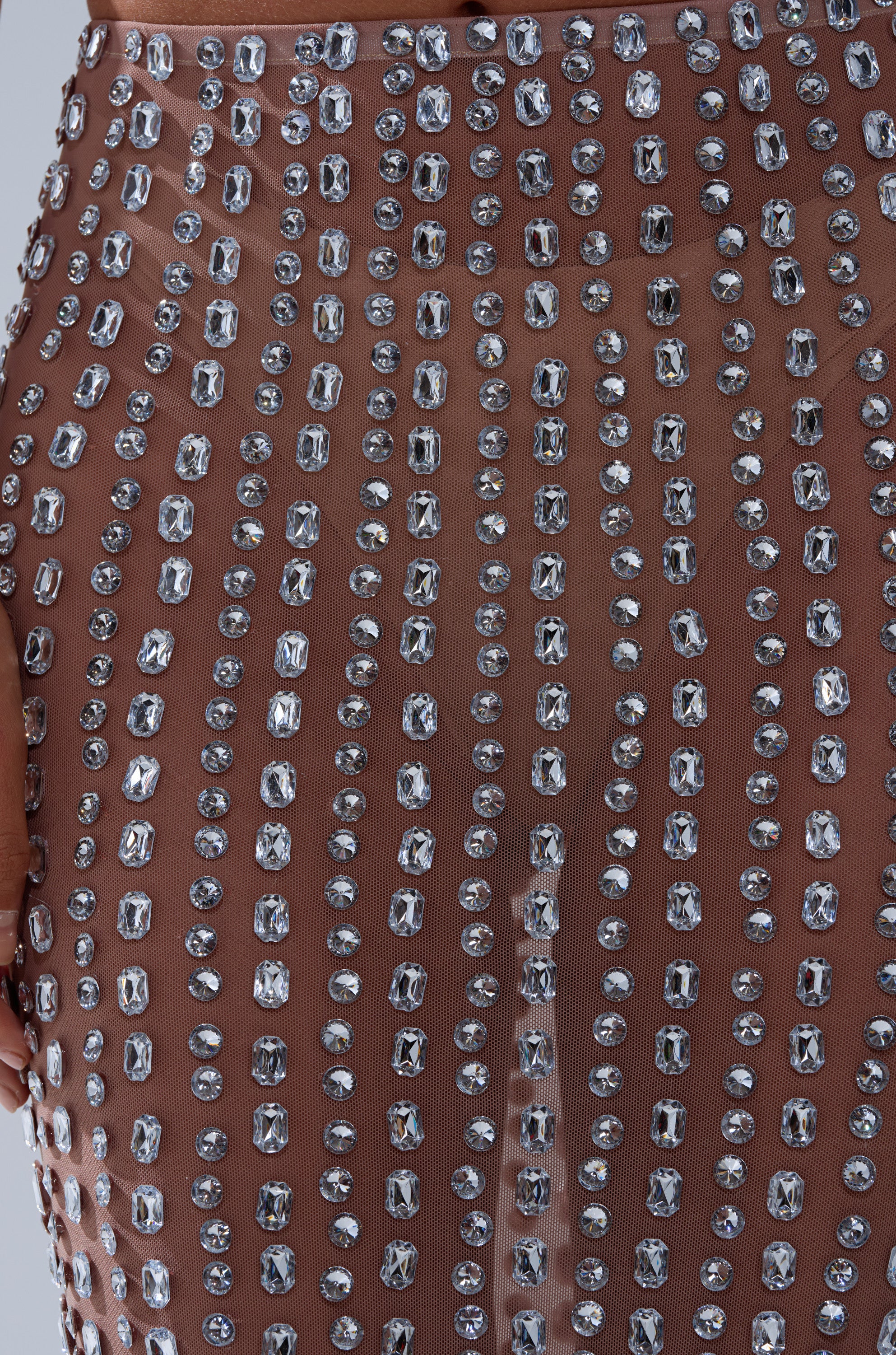 Close-up of the ALL THE SHINE RHINESTONE MAXI SKIRT: a sheer, nude maxi skirt adorned with square and oval rhinestones on mesh fabric, creating a sparkling decorative pattern.