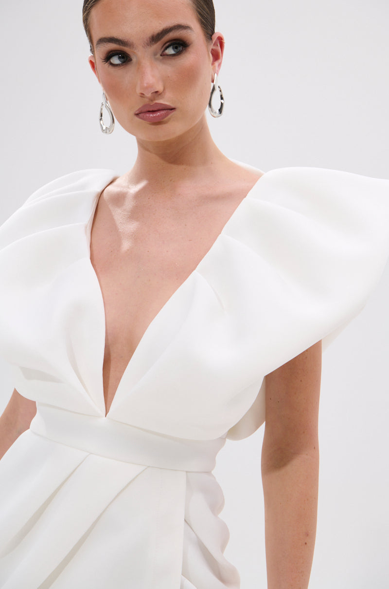 A woman wearing the Irreplaceable Ruffle Sleeve Tulip Hem Mini Dress in White, accessorized with large hoop earrings, looks to the side against a plain light background.