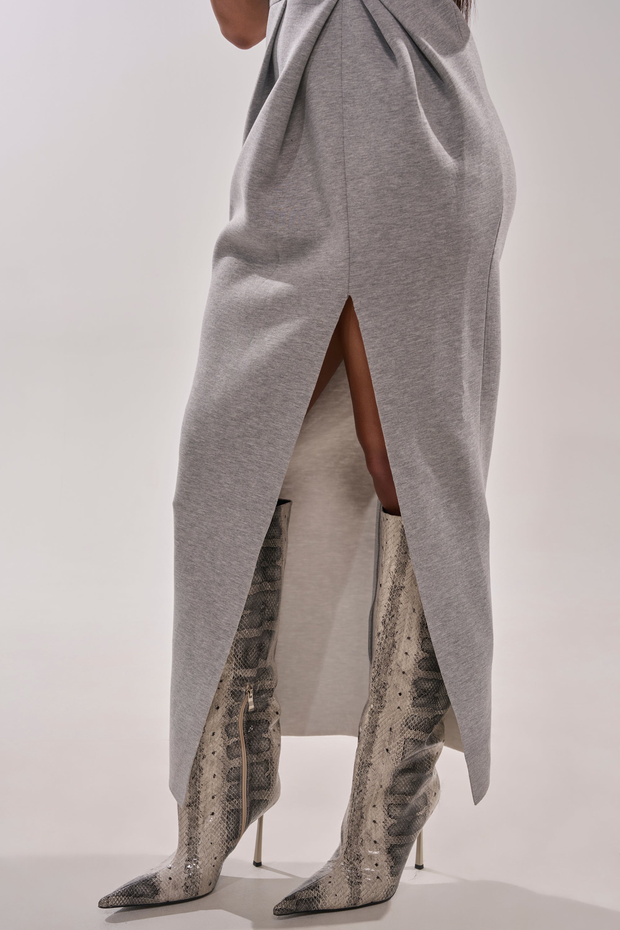 A person wearing the MAKE YOU MINE MAXI DRESS, styled with knee-high, pointed-toe, snakeskin boots and architectural shoulders, stands on a neutral background. 5