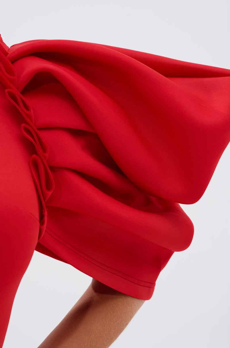 A close-up of a person wearing the PURE JOY MIDI DRESS WITH DRAMATIC SLEEVE IN RED, featuring vibrant red fabric and voluminous ruffled sleeves, set against a plain light background.