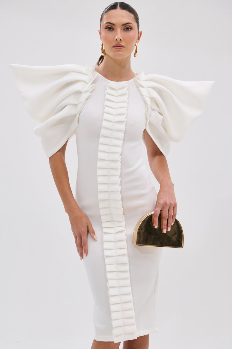 A woman wears the PURE JOY MIDI DRESS WITH DRAMATIC SLEEVE IN WHITE, featuring bold ruffled sleeves and a front ruffle detail. She holds a gold half-moon clutch and stands against a plain white background.